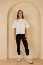 Woman wearing a white t-shirt and black leggings standing in front of a beige archway.